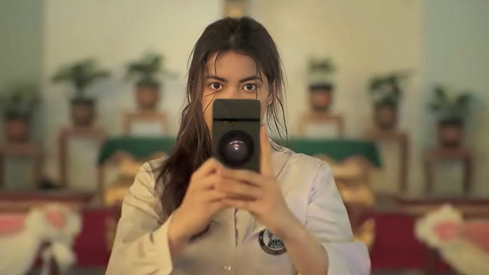 Charada Imrapornn pointing a black camera phone directly at the frame in a scene from the Thai series Delete